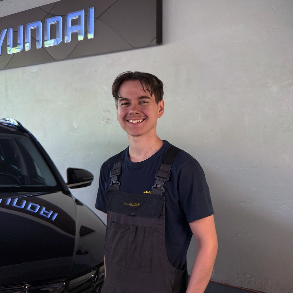 Luca Schmidiger von der Touring Garage Brünisholz in Escholzmatt im dunklen le GARAGE Arbeitsoverall vor dem Hyundai-Logo.