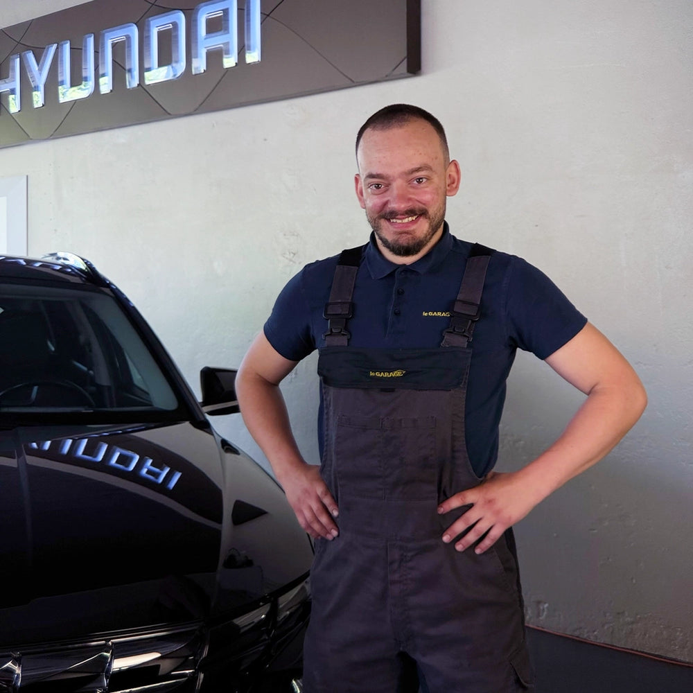 Robin Vogel von der Touring Garage Brünisholz in Escholzmatt im dunklen le GARAGE Arbeitsoverall vor dem Hyundai-Logo.